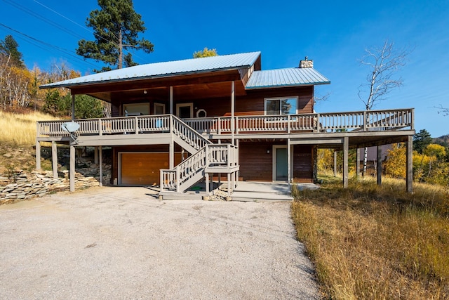 view of front of property featuring a wooden deck, metal roof, stone siding, an attached garage, and a chimney