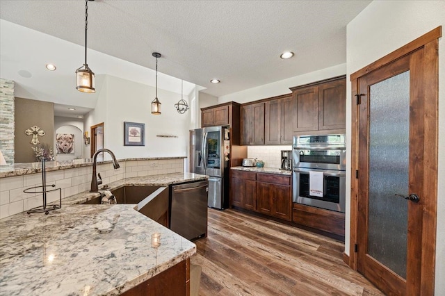 kitchen featuring stainless steel appliances, light stone counters, sink, and hardwood / wood-style flooring