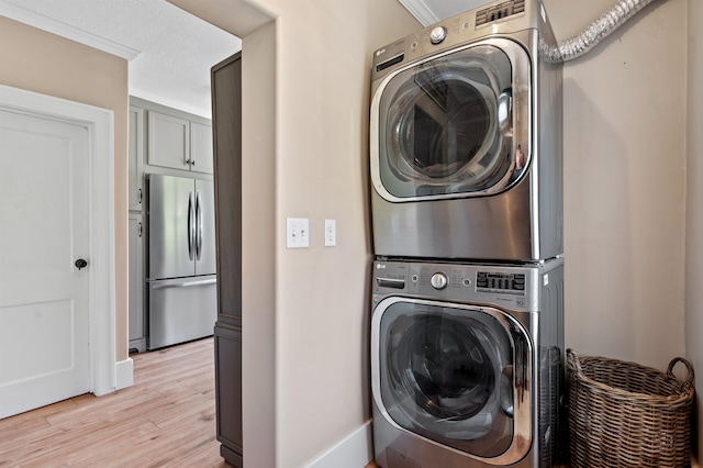 clothes washing area featuring stacked washer and dryer, light hardwood / wood-style floors, crown molding, and a textured ceiling