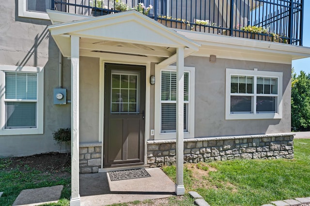 view of exterior entry with a lawn and a balcony