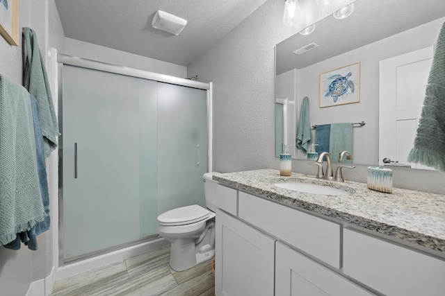 bathroom featuring an enclosed shower, hardwood / wood-style flooring, toilet, vanity, and a textured ceiling