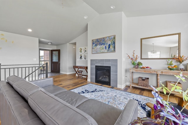 living room with hardwood / wood-style flooring, a tiled fireplace, and vaulted ceiling