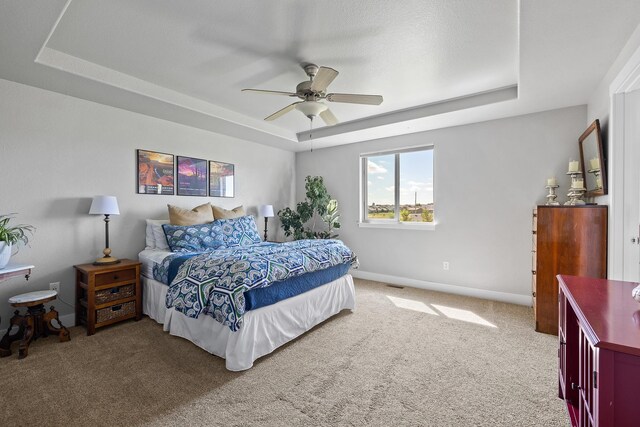 bedroom with a raised ceiling, ceiling fan, and carpet floors