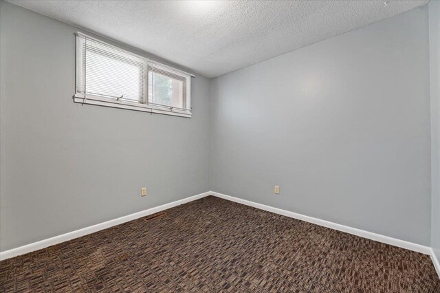 spare room with a textured ceiling and dark colored carpet