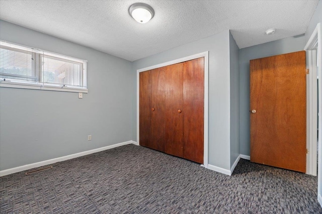 unfurnished bedroom featuring a textured ceiling, dark carpet, and a closet