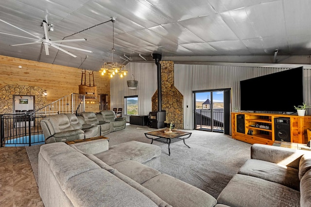 living room featuring wood walls, ceiling fan, a wood stove, and carpet floors