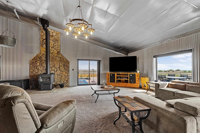 carpeted living room with a wood stove, a notable chandelier, and vaulted ceiling