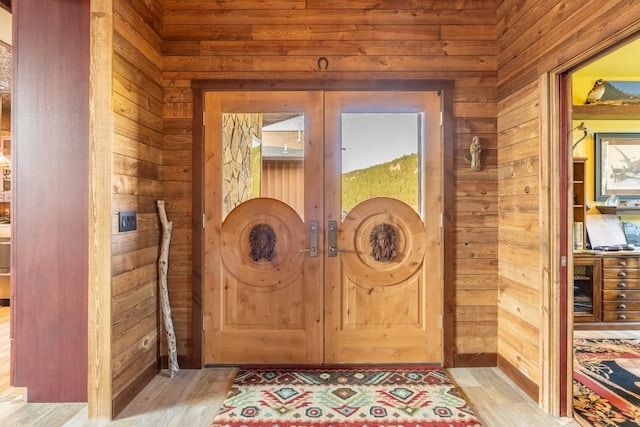 entryway with light wood-type flooring, wood walls, and french doors