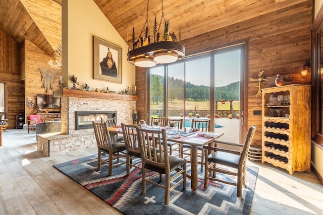 dining space with wood-type flooring, a stone fireplace, wooden walls, and high vaulted ceiling