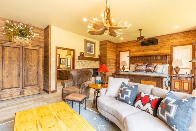 living room with ceiling fan with notable chandelier, wooden walls, light hardwood / wood-style floors, and a fireplace