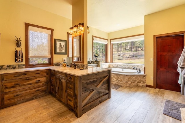 bathroom featuring wood-type flooring, vanity, and a relaxing tiled tub