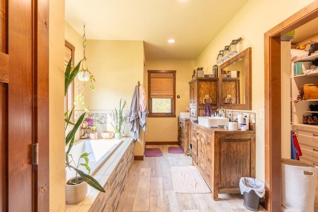 bathroom with a relaxing tiled tub, vanity, and hardwood / wood-style flooring