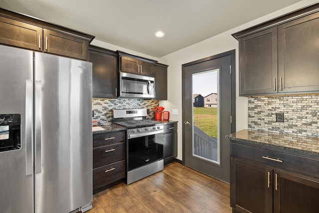 kitchen featuring decorative backsplash, dark hardwood / wood-style flooring, stainless steel appliances, dark brown cabinets, and dark stone counters