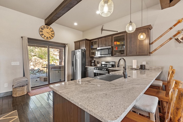 kitchen with appliances with stainless steel finishes, a kitchen breakfast bar, kitchen peninsula, dark hardwood / wood-style flooring, and pendant lighting