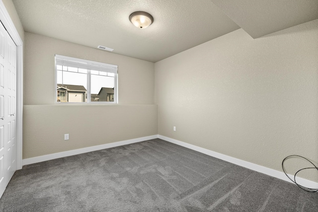 spare room featuring dark colored carpet and a textured ceiling