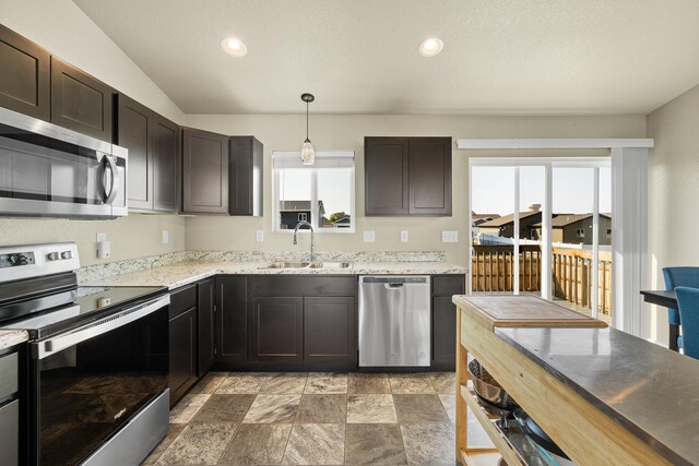 kitchen featuring dark brown cabinets, sink, vaulted ceiling, stainless steel appliances, and decorative light fixtures