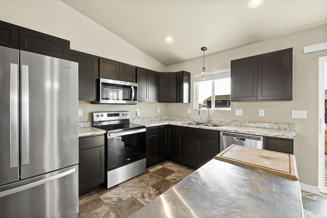 kitchen with light stone counters, sink, lofted ceiling, hanging light fixtures, and appliances with stainless steel finishes