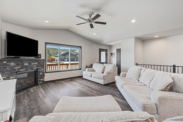 living room with ceiling fan, a stone fireplace, lofted ceiling, and dark wood-type flooring