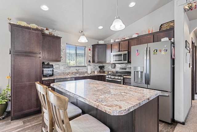 kitchen with dark brown cabinets, stainless steel appliances, a center island, vaulted ceiling, and decorative backsplash