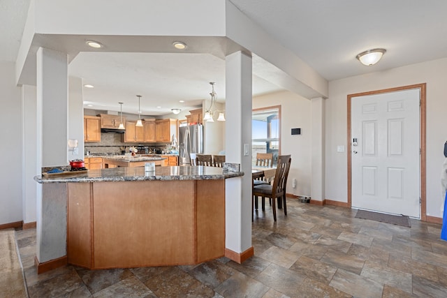 kitchen featuring hanging light fixtures, kitchen peninsula, stainless steel refrigerator, dark stone counters, and decorative backsplash