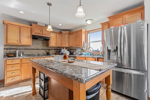 kitchen with dark stone counters, pendant lighting, tasteful backsplash, a kitchen island, and stainless steel fridge