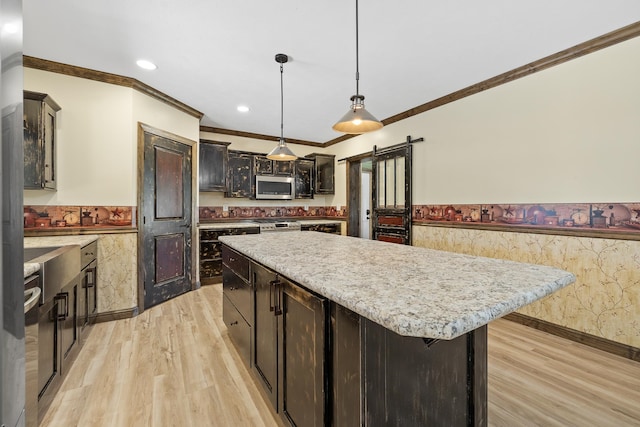 kitchen featuring a kitchen island, light wood-type flooring, a barn door, appliances with stainless steel finishes, and decorative light fixtures