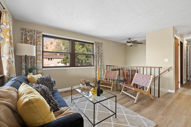 living room featuring ceiling fan, a textured ceiling, and light wood-type flooring