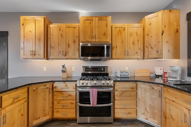 kitchen with light brown cabinets, stainless steel appliances, and dark stone countertops