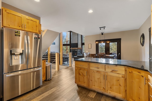 kitchen featuring a warm lit fireplace, dark wood-type flooring, stainless steel refrigerator with ice dispenser, dark stone counters, and decorative light fixtures