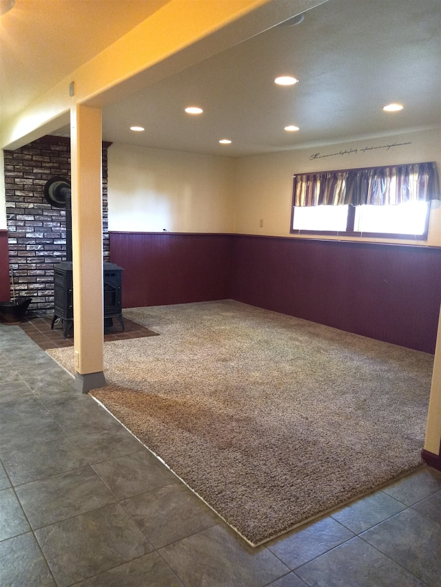 basement featuring a wood stove, wooden walls, and dark carpet