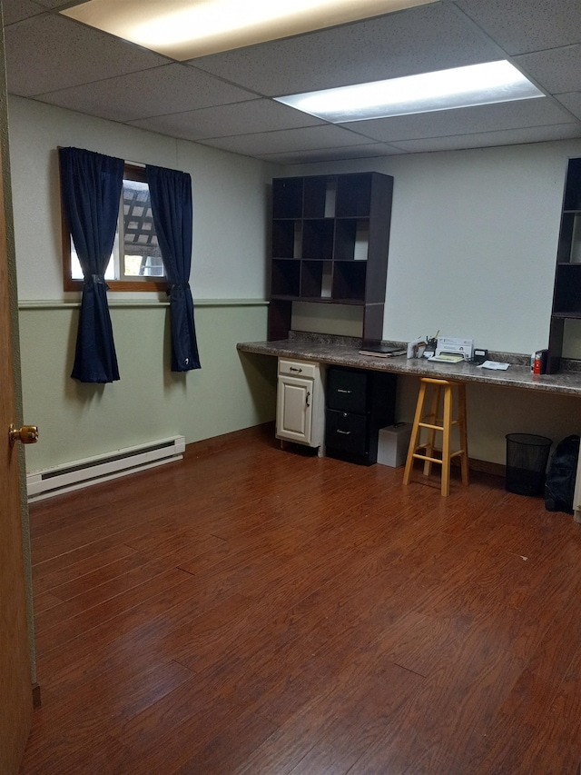 home office featuring dark hardwood / wood-style flooring, a paneled ceiling, a baseboard radiator, and built in desk