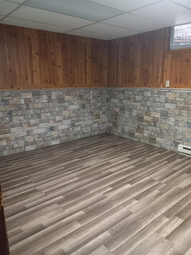 basement featuring a drop ceiling, wood walls, and hardwood / wood-style floors