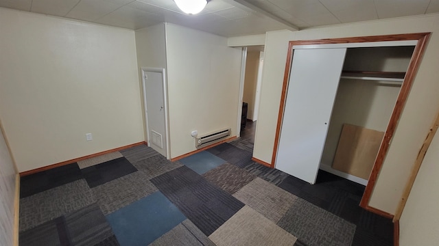 unfurnished bedroom featuring dark colored carpet, a closet, and a baseboard heating unit