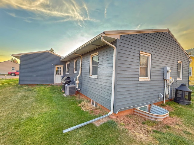 property exterior at dusk with a yard and cooling unit