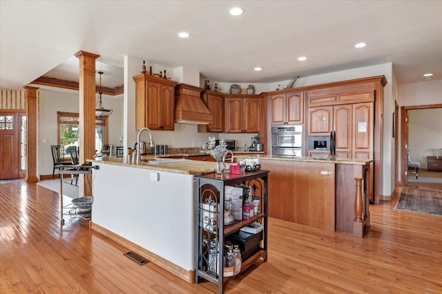 kitchen featuring custom range hood, light hardwood / wood-style floors, decorative columns, and kitchen peninsula