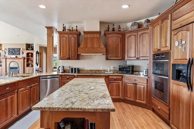 kitchen with light stone countertops, appliances with stainless steel finishes, sink, a kitchen island, and light hardwood / wood-style flooring