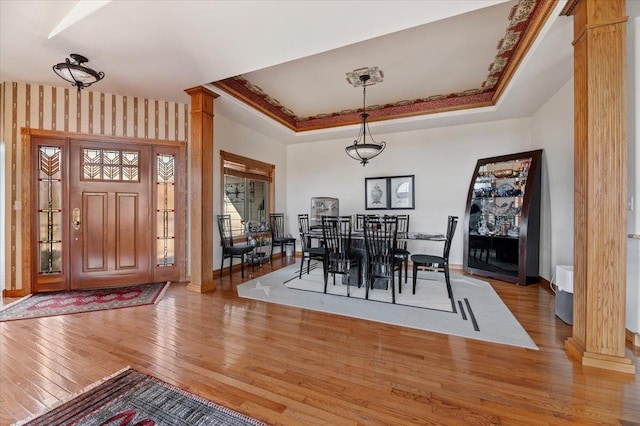 dining room with light hardwood / wood-style floors, a tray ceiling, and decorative columns