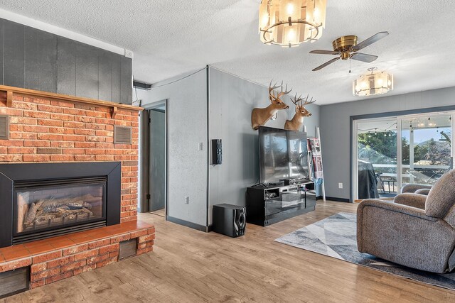 living room featuring light hardwood / wood-style floors, a brick fireplace, a textured ceiling, and ceiling fan