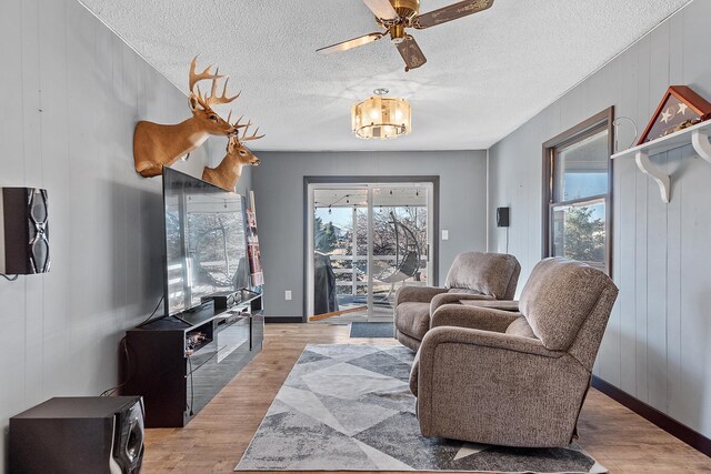 living room with ceiling fan, a textured ceiling, and light wood-type flooring