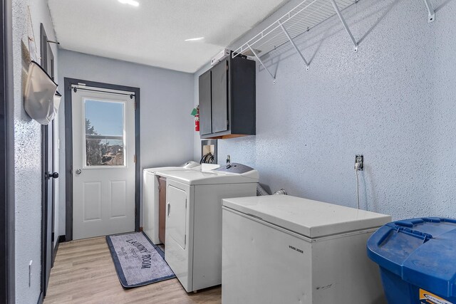 clothes washing area with a textured ceiling, cabinets, light wood-type flooring, and washing machine and clothes dryer