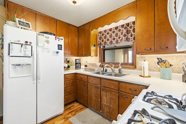 kitchen featuring sink, light wood-type flooring, white appliances, and tasteful backsplash