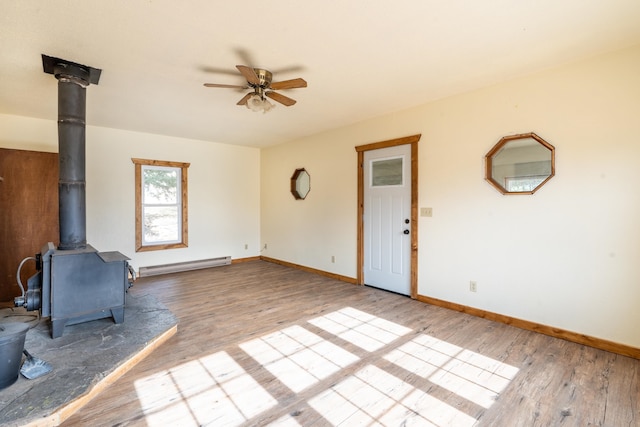 unfurnished living room featuring light hardwood / wood-style floors, a wood stove, baseboard heating, and ceiling fan