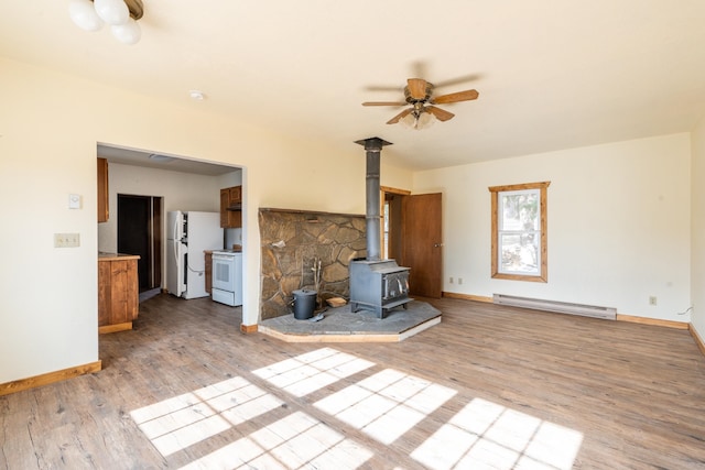 unfurnished living room featuring light hardwood / wood-style floors, a wood stove, baseboard heating, and ceiling fan