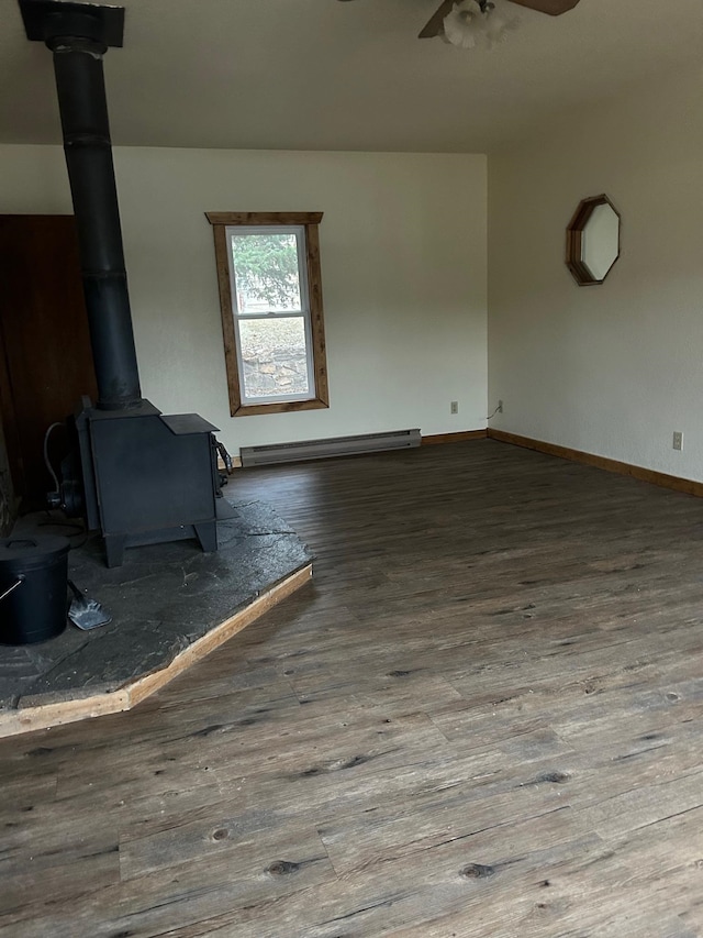 unfurnished living room with ceiling fan, a wood stove, dark hardwood / wood-style flooring, and a baseboard heating unit