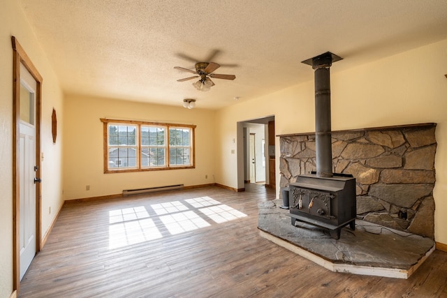 living room with a wood stove, hardwood / wood-style floors, baseboard heating, and a textured ceiling