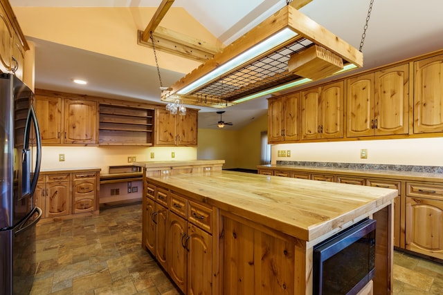 kitchen featuring butcher block counters, stainless steel fridge, built in microwave, a center island, and decorative light fixtures