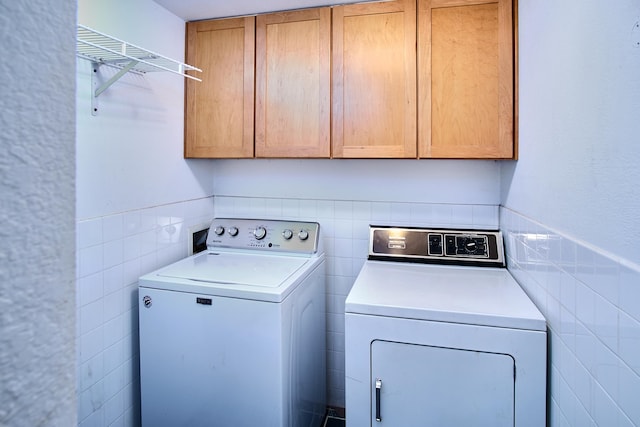 laundry room featuring tile walls, independent washer and dryer, and cabinets