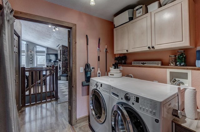 clothes washing area featuring cabinets, a textured ceiling, washing machine and clothes dryer, and light wood-type flooring