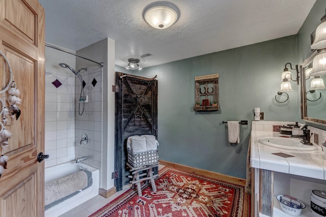 bathroom featuring vanity, a textured ceiling, tile patterned flooring, and tiled shower / bath