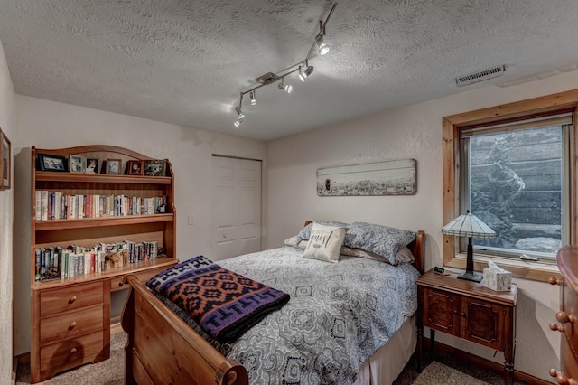 bedroom with a closet, carpet flooring, a textured ceiling, and track lighting